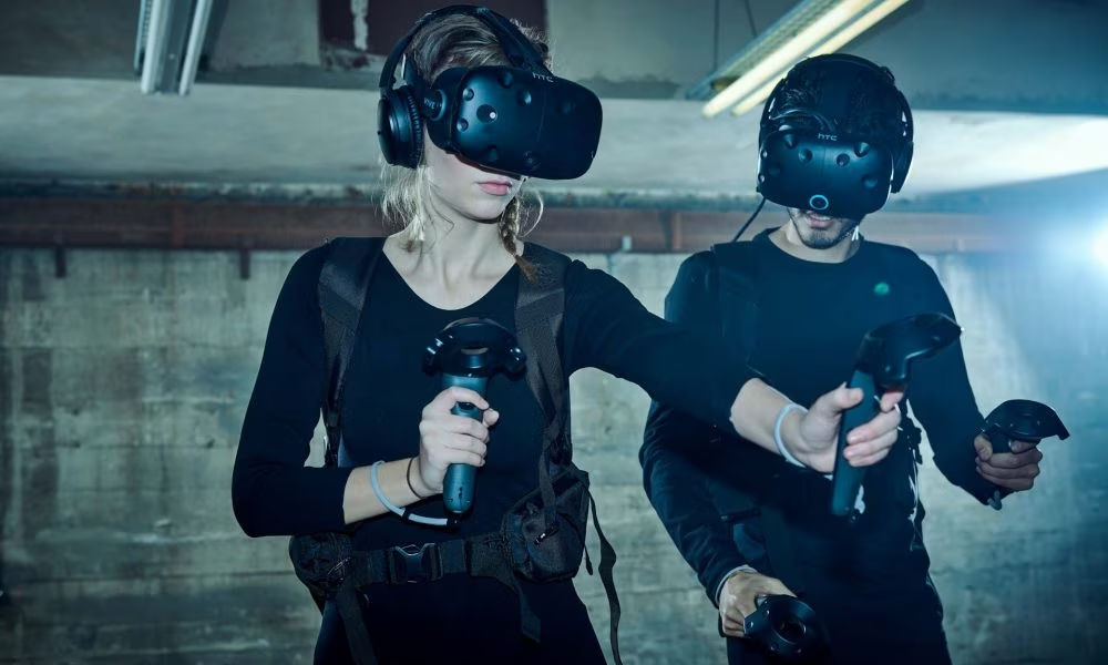 A photo of two VR uses with headsets on and using controllers inside a warehouse-looking room.